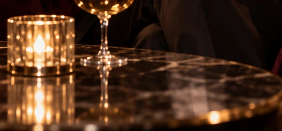 Mesa de lounge em mármore com uma taça e uma vela acesa, em luz quente.